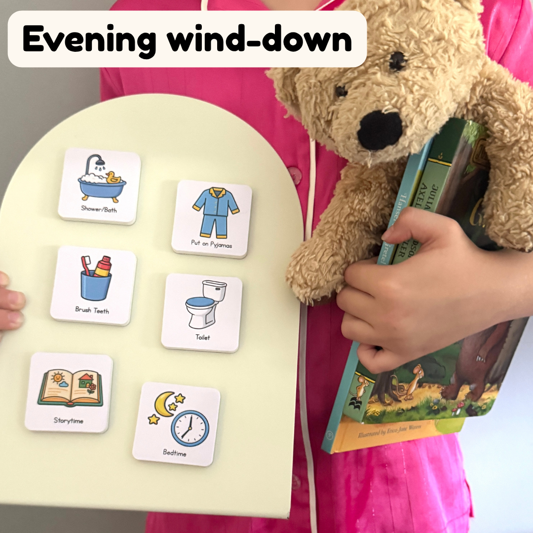 Child holding a book with a teddy bear and bedtime routine magnets on a cream magnetic board.