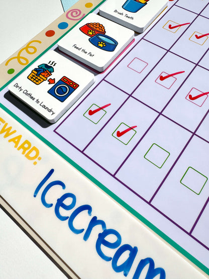 Close-up of a children's daily routine chart board with colourful icons and text, including 'My Reward:' and 'Ice cream,' alongside task magnets showing actions like 'Dirty Clothes to Laundry' and 'Feed the Pet.'.