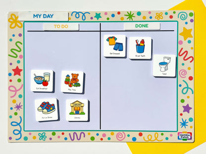 A children's daily planning magnetic board with colourful decorative border, a 'MY DAY' header, and columns labelled 'TO DO' and 'DONE'. Magnetic activity tiles showing breakfast, play time, shoes, library, clothes, brush teeth, and toilet are arranged on the board.