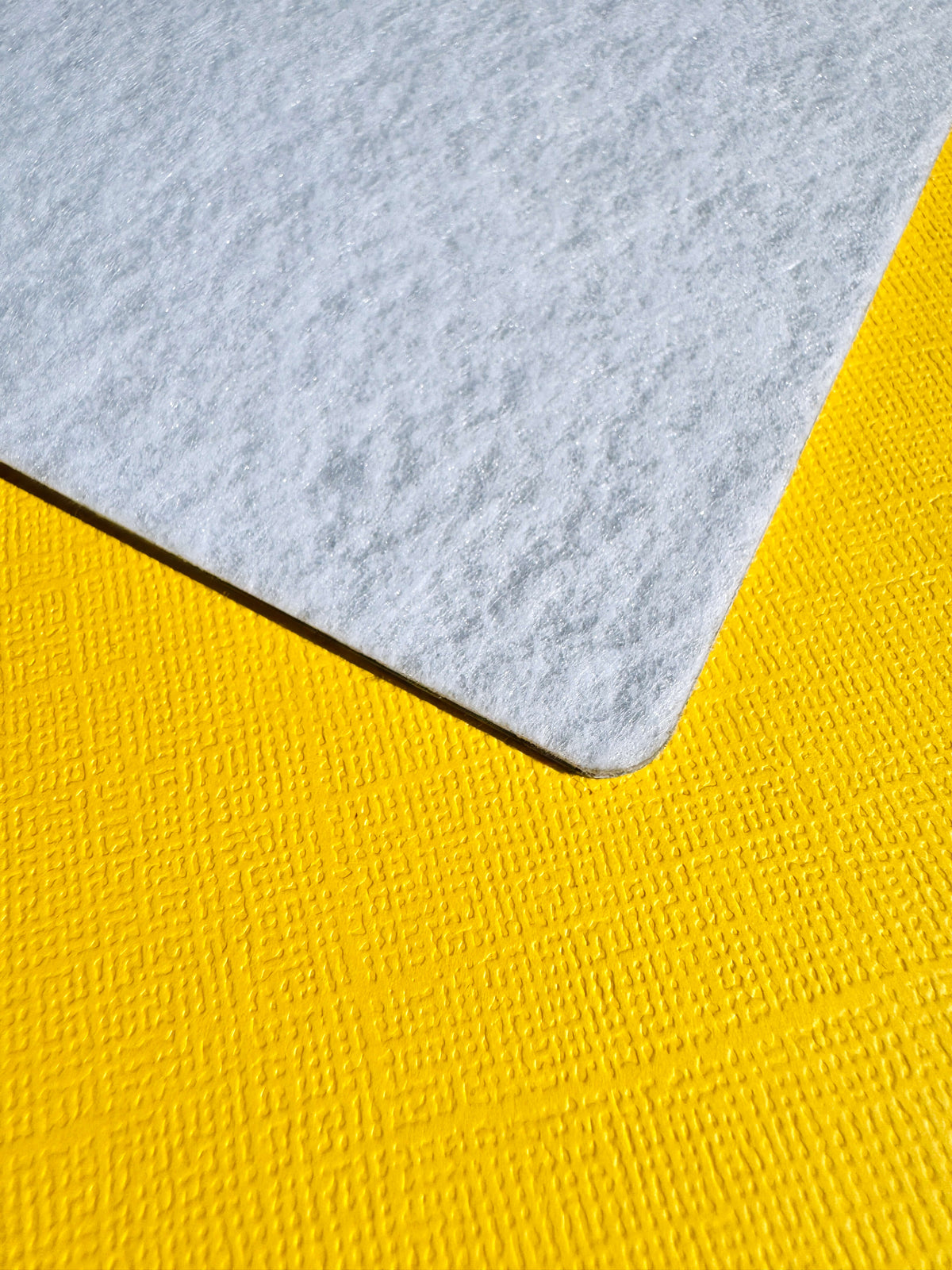 A close-up of the back of the Flex & Flow magnetic board showing a light grey felt material corner placed on top of a textured yellow surface.