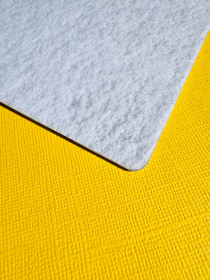 A close-up of the back of the Flex & Flow magnetic board showing a light grey felt material corner placed on top of a textured yellow surface.