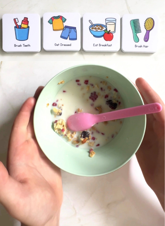 Person holding a bowl of cereal with a pink spoon, with routine magnets in the background.