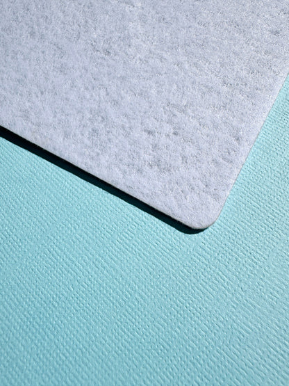 A close-up of the back of the Tick & Track magnetic board showing a light grey felt material corner placed on top of a textured aqua surface.