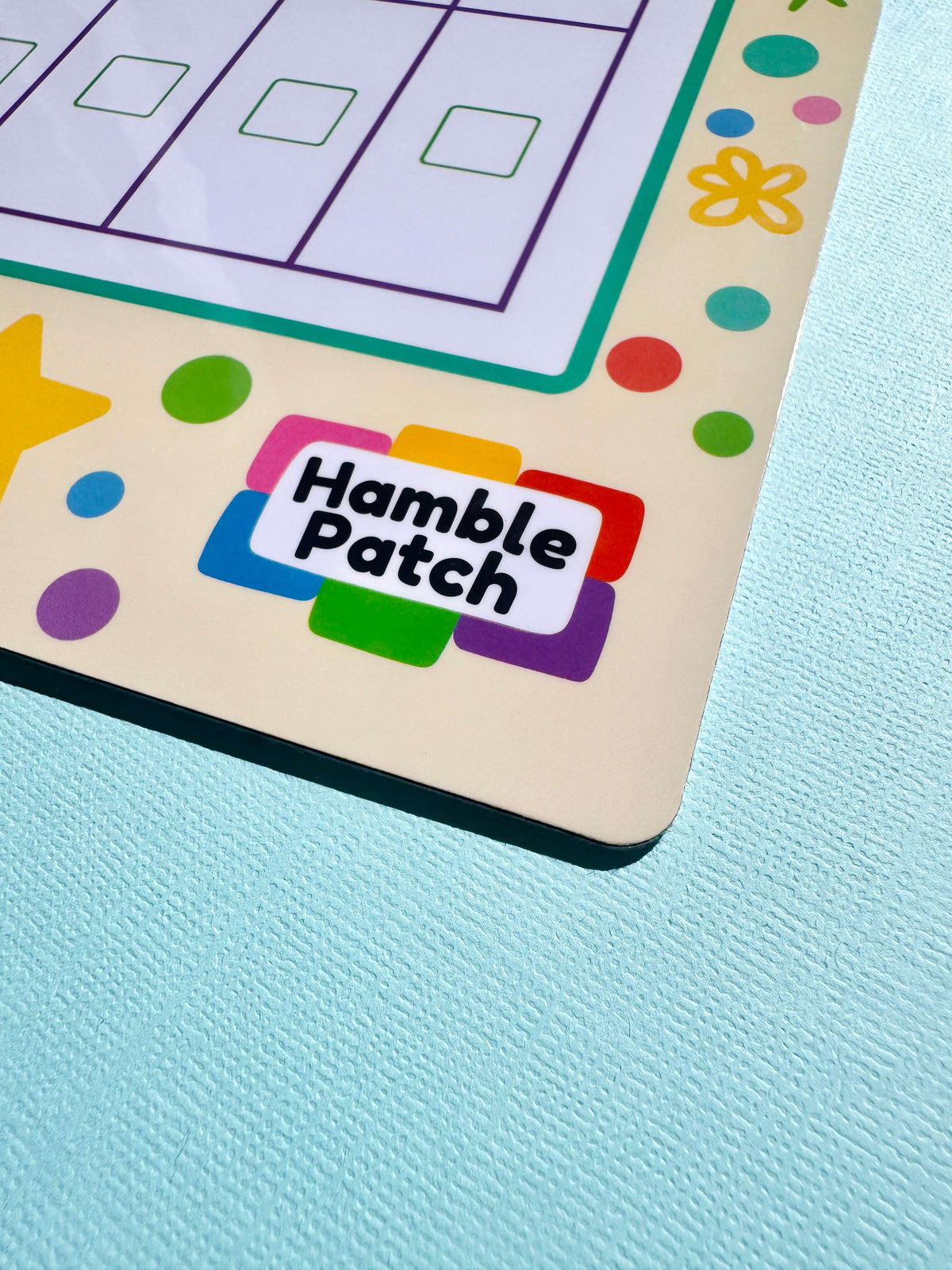 A close-up of a colourful printed magnetic board featuring the logo 'Hamble Patch' in black on a white label with multi-coloured border shapes, placed on a light blue textured surface.